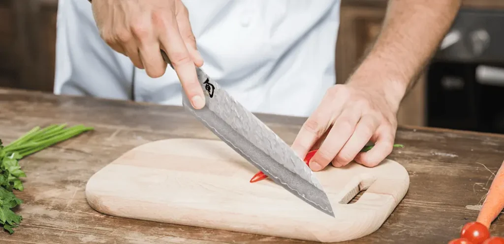 Chef cortando vegetales con un cuchillo para chef profesional Shun Premier en una tabla para picar con una cocina de fondo