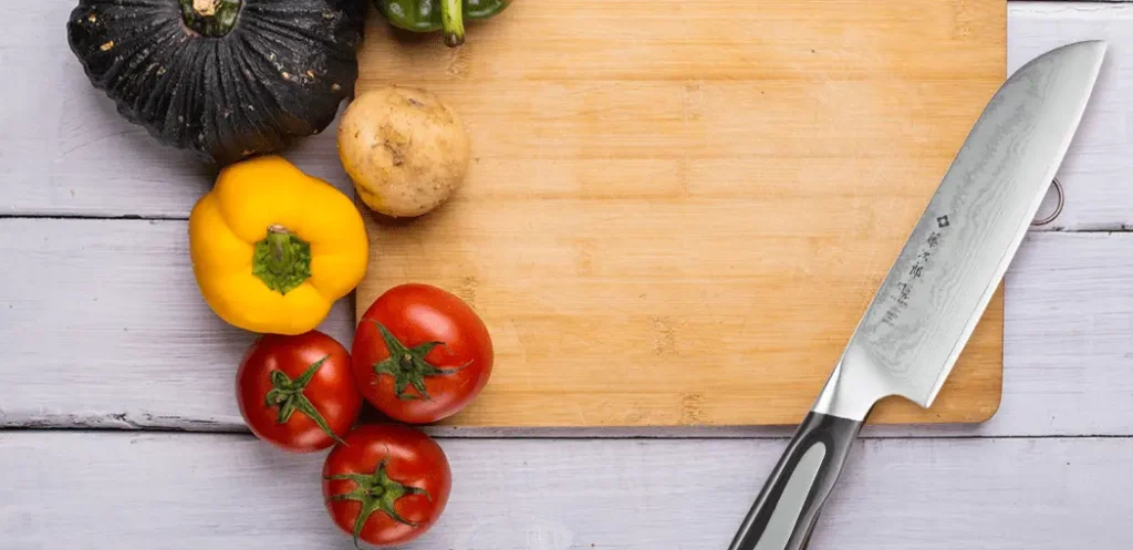 Cuchillo para chef profesional Tojiro DP sobre una tabla de picar con vegetales encima