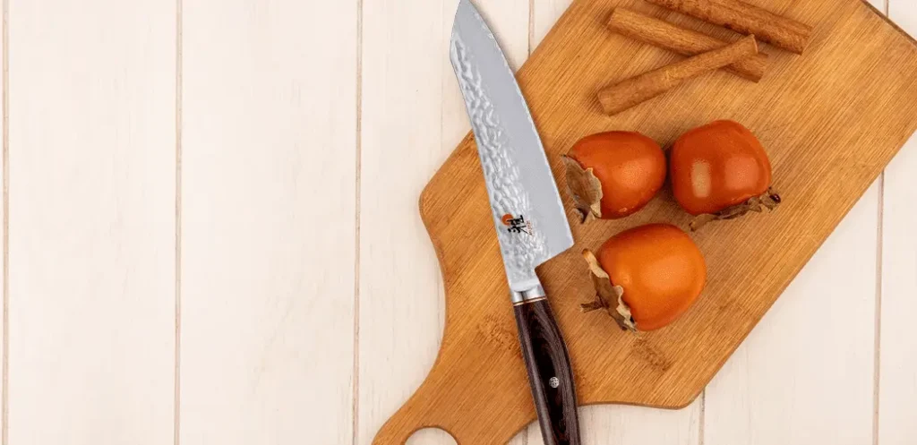 Cuchillo para chef profesional Miyabi Artisan sobre una tabla de picar con vegetales encima